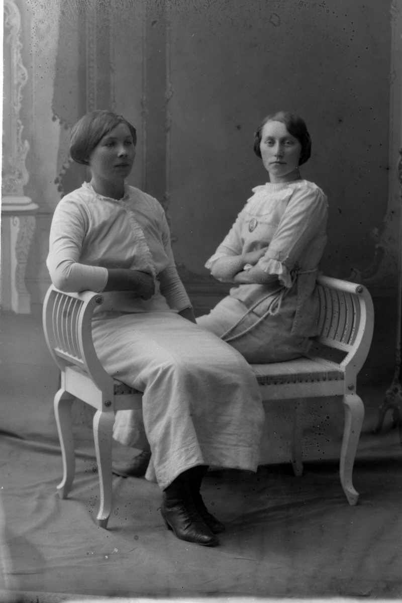 Studioportrett av to kvinner som sitter på en benk.