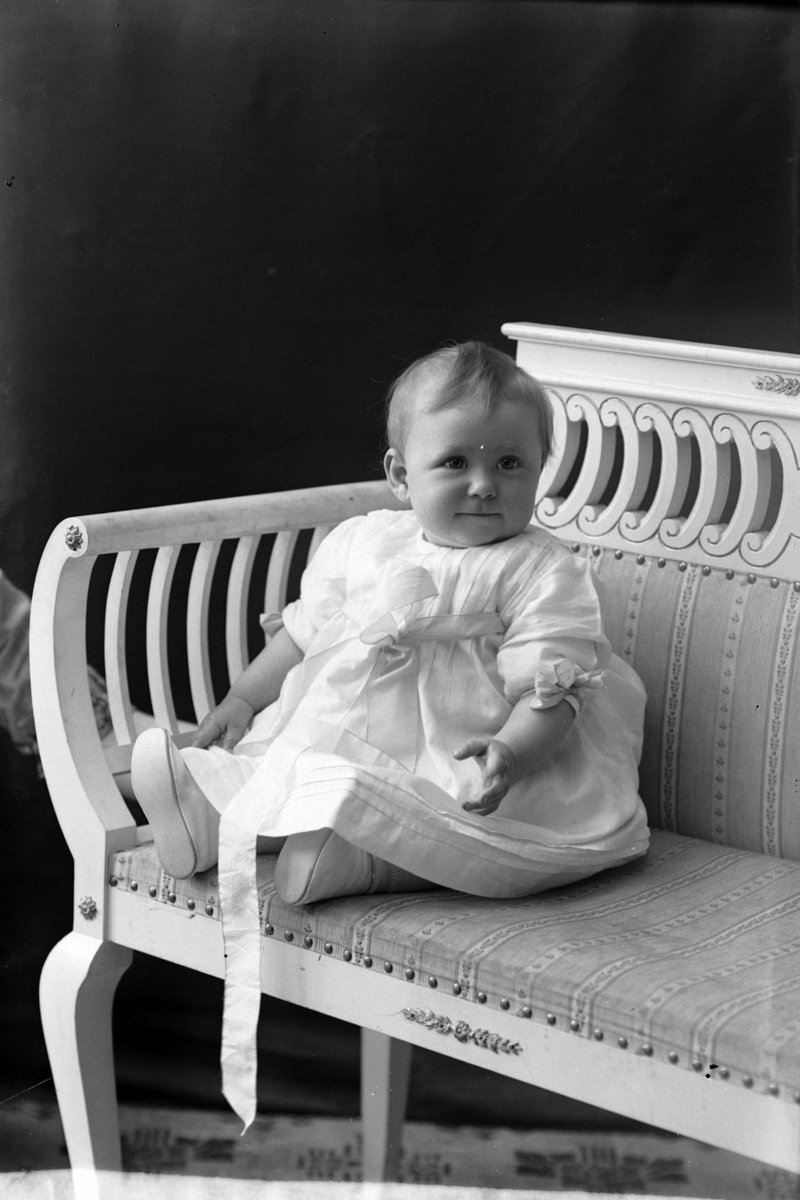 Studioportrett av et lite barn i en hvit kjole.