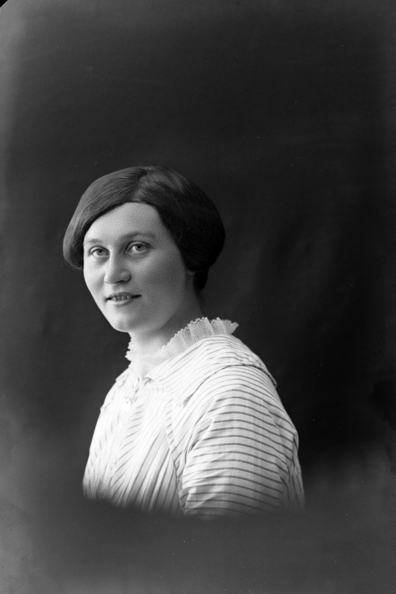 Studioportrett i halvfigur av kvinne med stripet skjorte.
