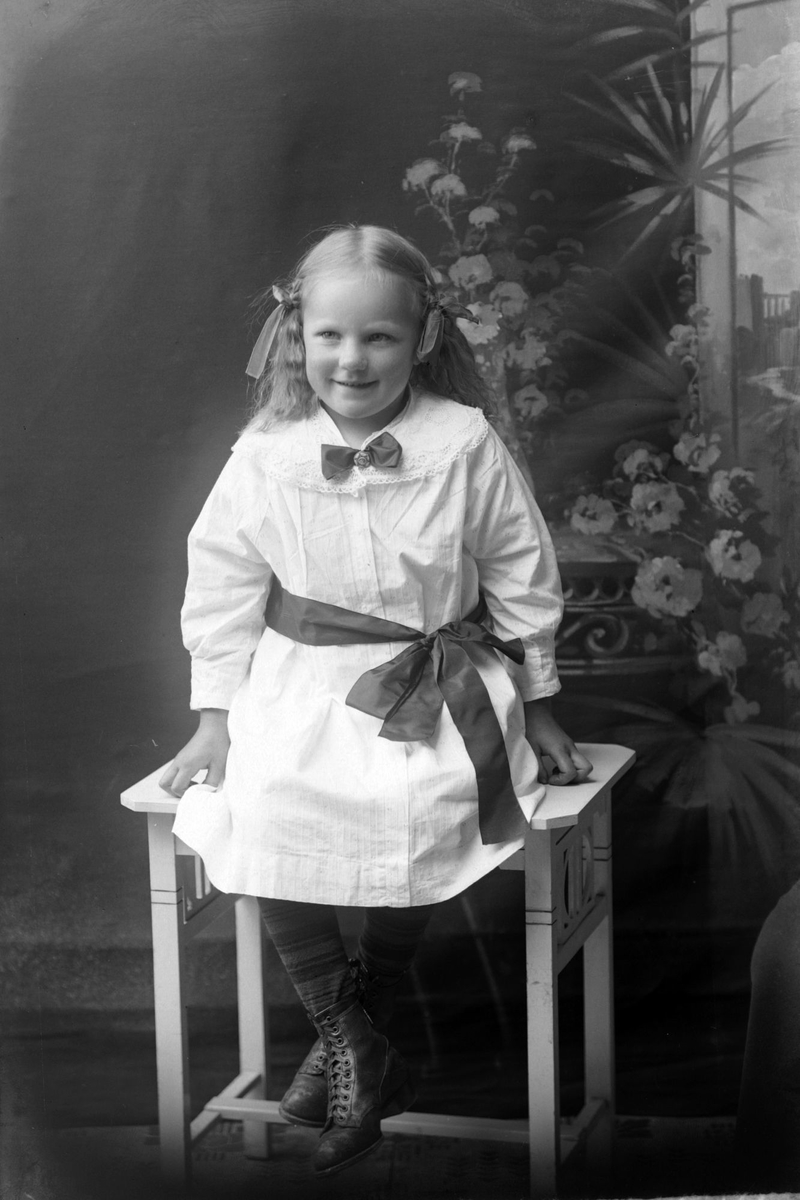 Studioportrett av en jente i hvit kjole med sløyfer i håret.