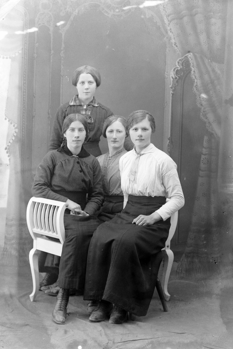 Studioportrett av tre sittende kvinner foran én som står.
