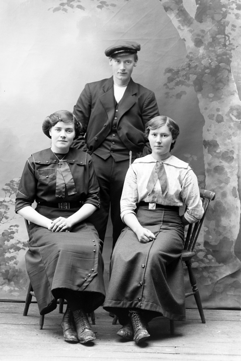 Studioportrett av to kvinner sittende foran en mann som står.