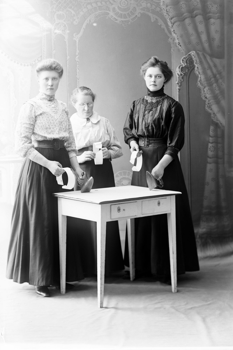 Studioportrett av tre kvinner med strykejern og løssnipper.