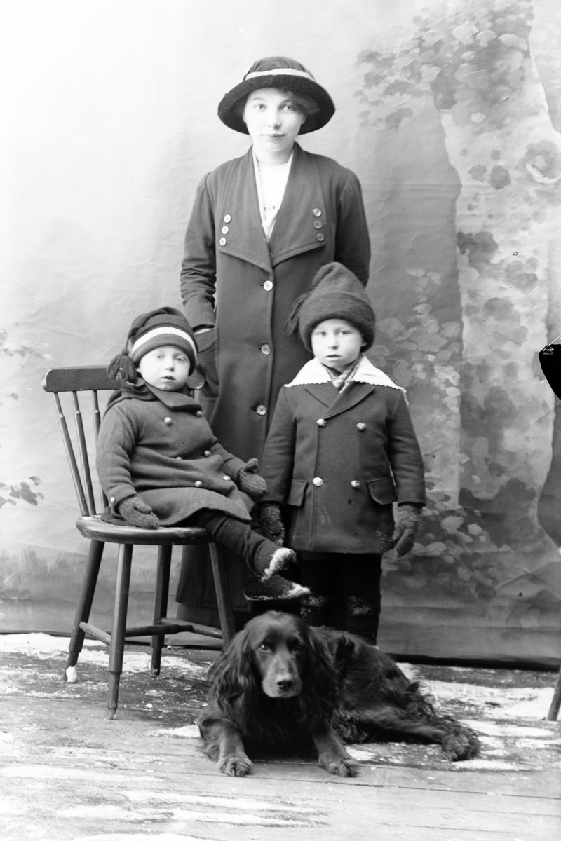 Studioportrett av en kvinne, to barn og en hund i helfigur.