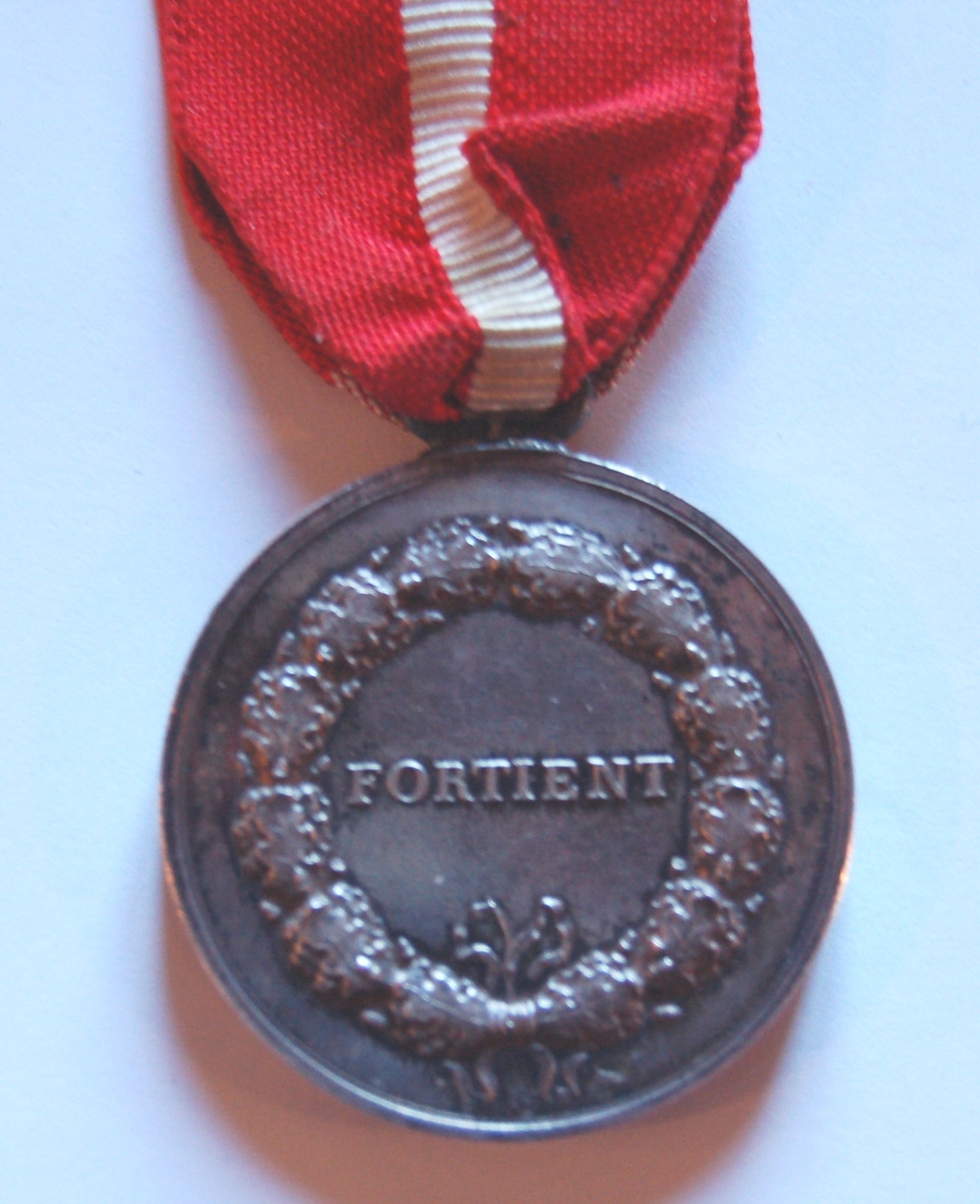Rund medaljong med sløyfe med hvitt kors på rød bunn