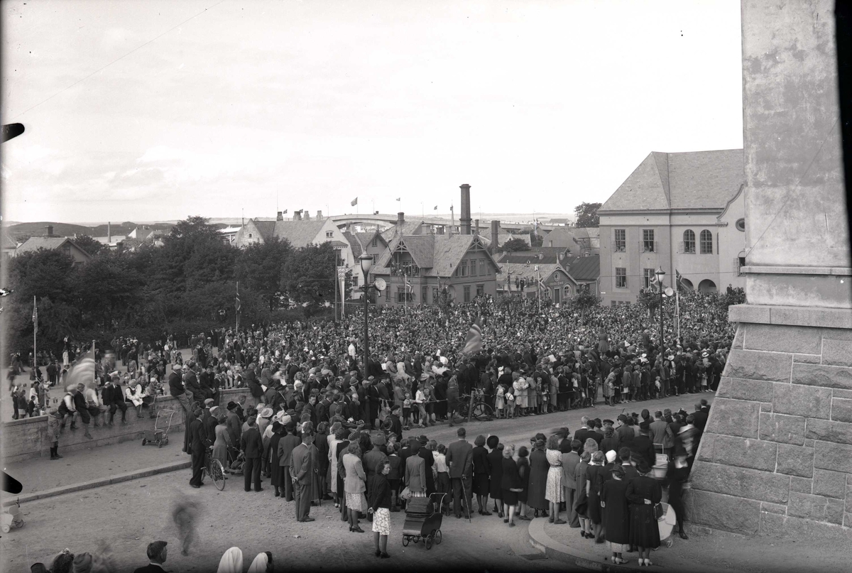 Stor folkemengde samlet foran Rådhuset. Gata er avsperret og folk står samlet bak tausperringene. I bakgrunnen til h. ses Festiviteten. Fra kong Haakon den 7.s besøk i Haugesund, 22.08.45.
