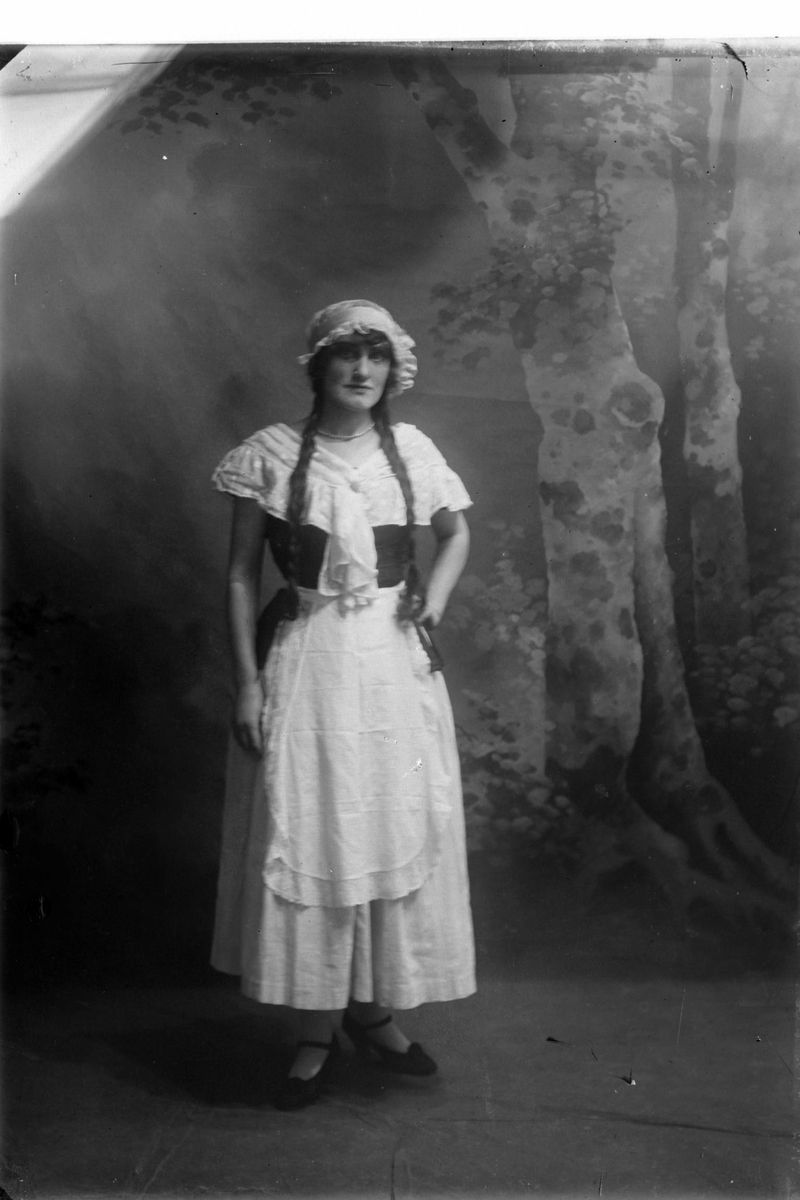 Studioportrett av en kvinne (?) med fletter og kostyme.