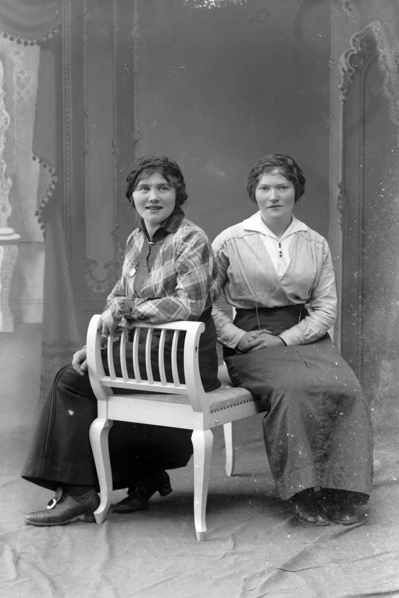 Studioportrett av to kvinner sittende på en benk.