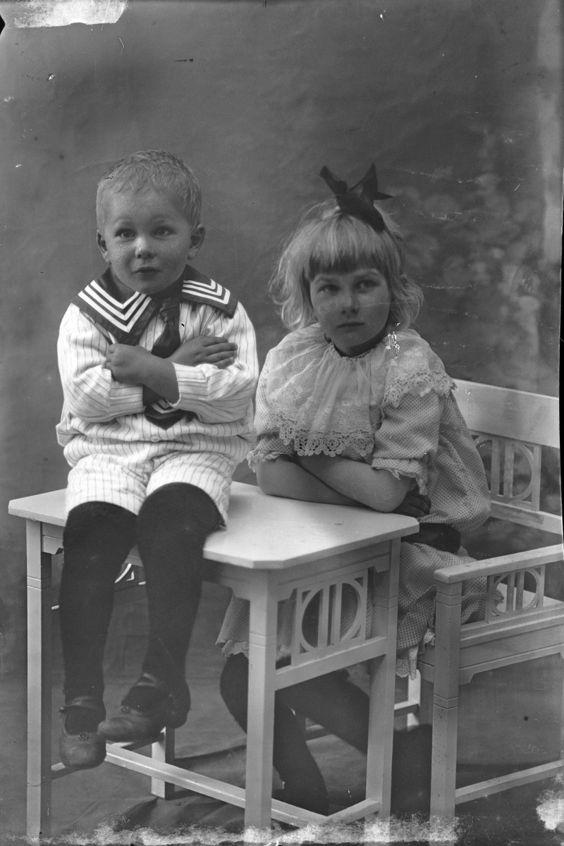 Studioportrett av to barn ved et bord og en stol.