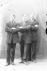 Studioportrett av tre menn med armene i kors.