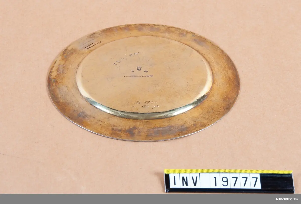 Förgylld paten. På undersidan märkt med åldermannaranka, dvs. paten tillverkad före 1754. H-årsbokstaven 1696, No 2 och 14 3/4 (kan vara lod) och år 1766. I mitten en svart hålihget 1x1 diameter, två avtryck av pung på undersidan. 