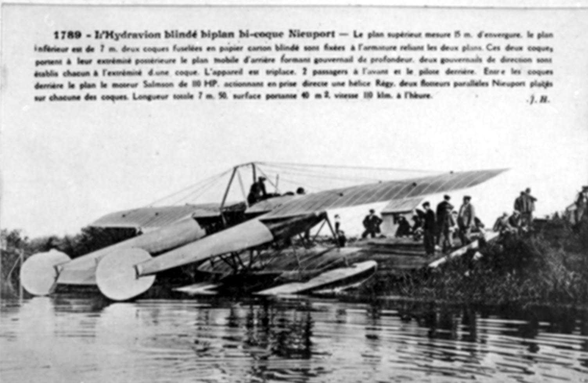 Ett fly ved vannkanten (slip), Nieuport.
En person i flyet, og flere personer ved flyet.