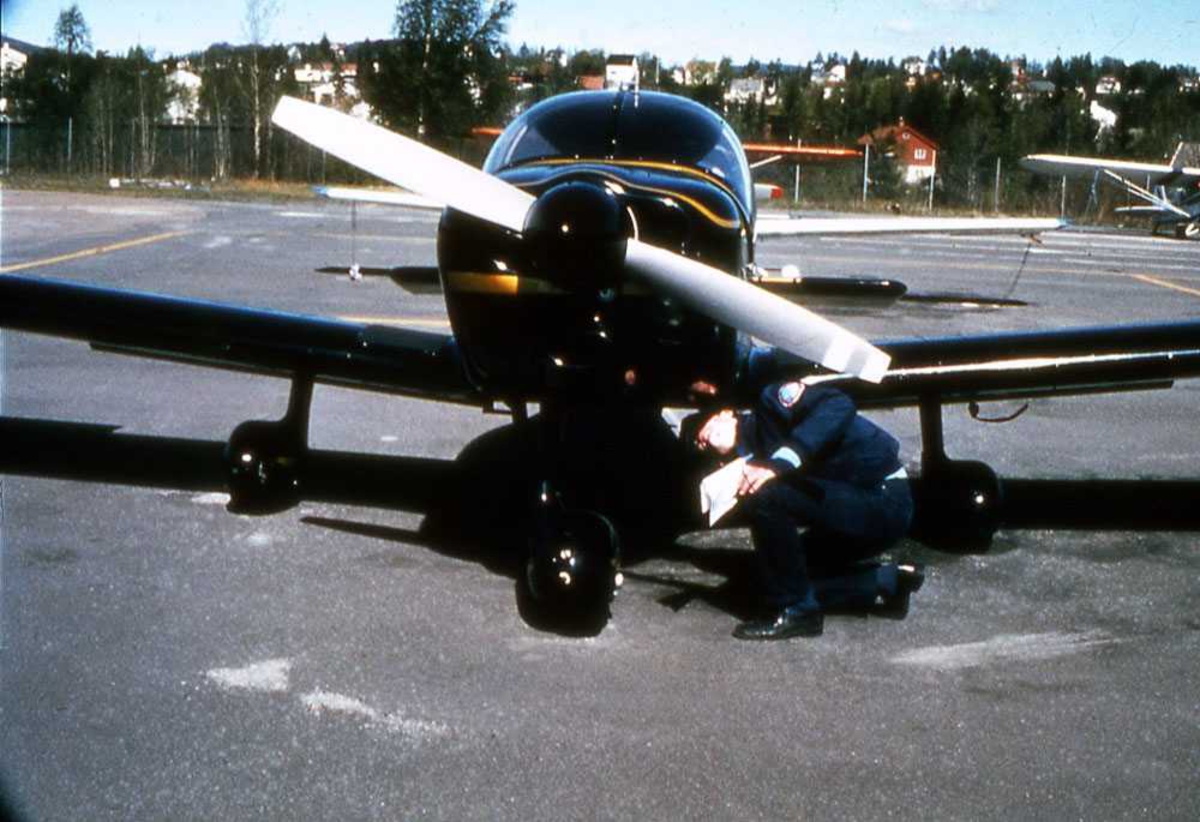 Ett fly på bakken. LN-RAC, Robin R.2160. En person ved fronten flyet. Inspeksjon. Småfly i bakgrunn.