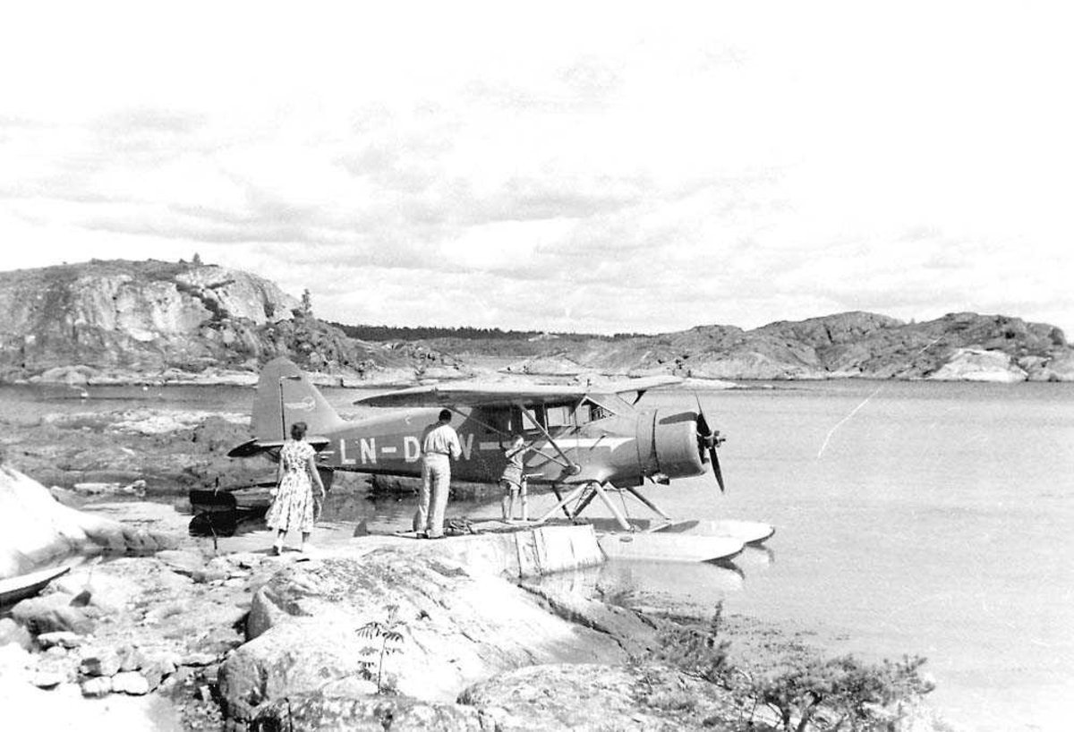 Ett fly som ligger fortøyd ved ei brygge, Polar C-5 LN-DBW fra Widerøe..Tre personer ved flyet. Fjell i bakgrunnen.