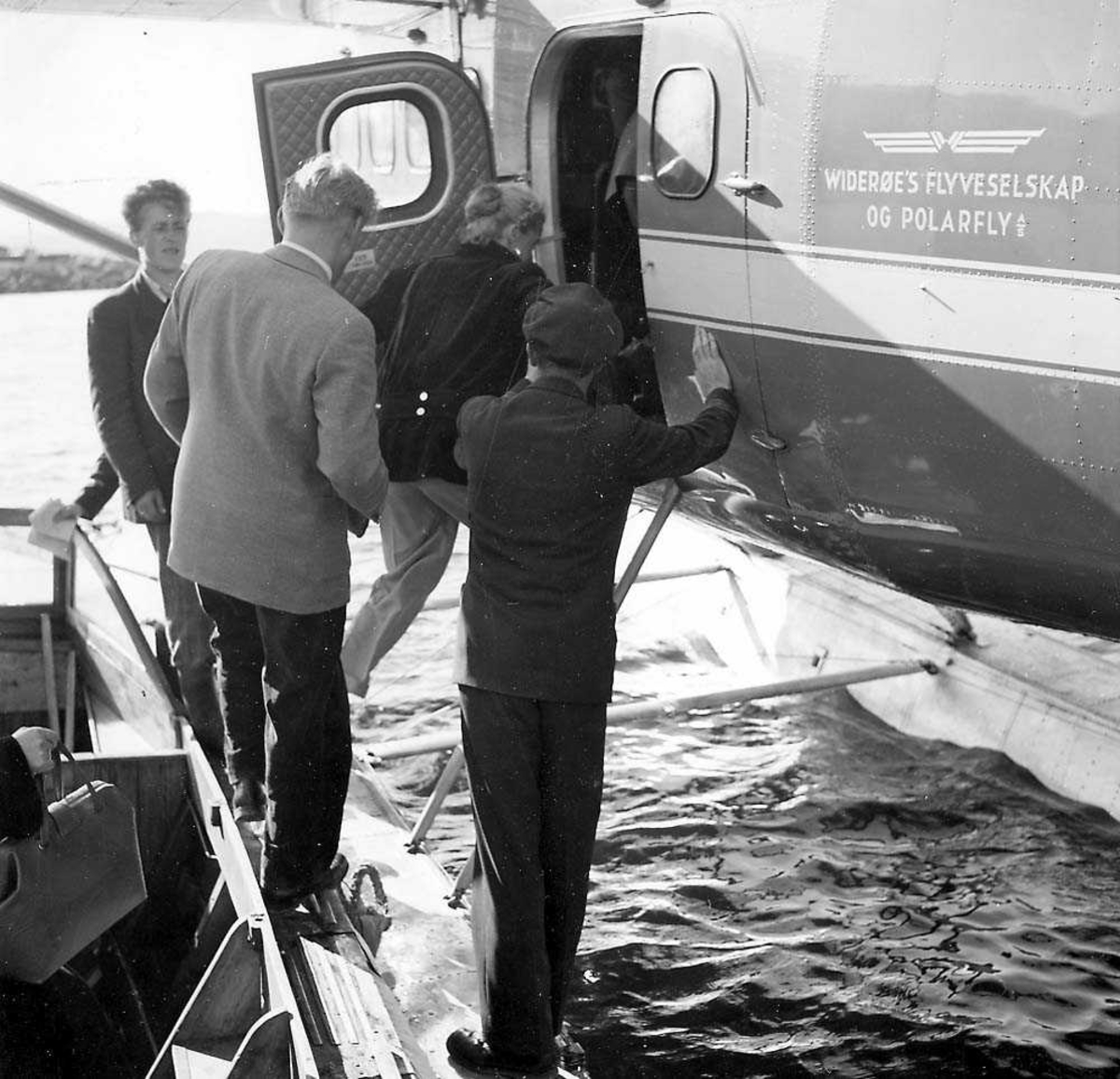 Flere passasjerer som klatrer ombord fra en båt til et sjøfly, DHC-3 Otter fra Widerøes Flyveselskap og Polarfly A/S.