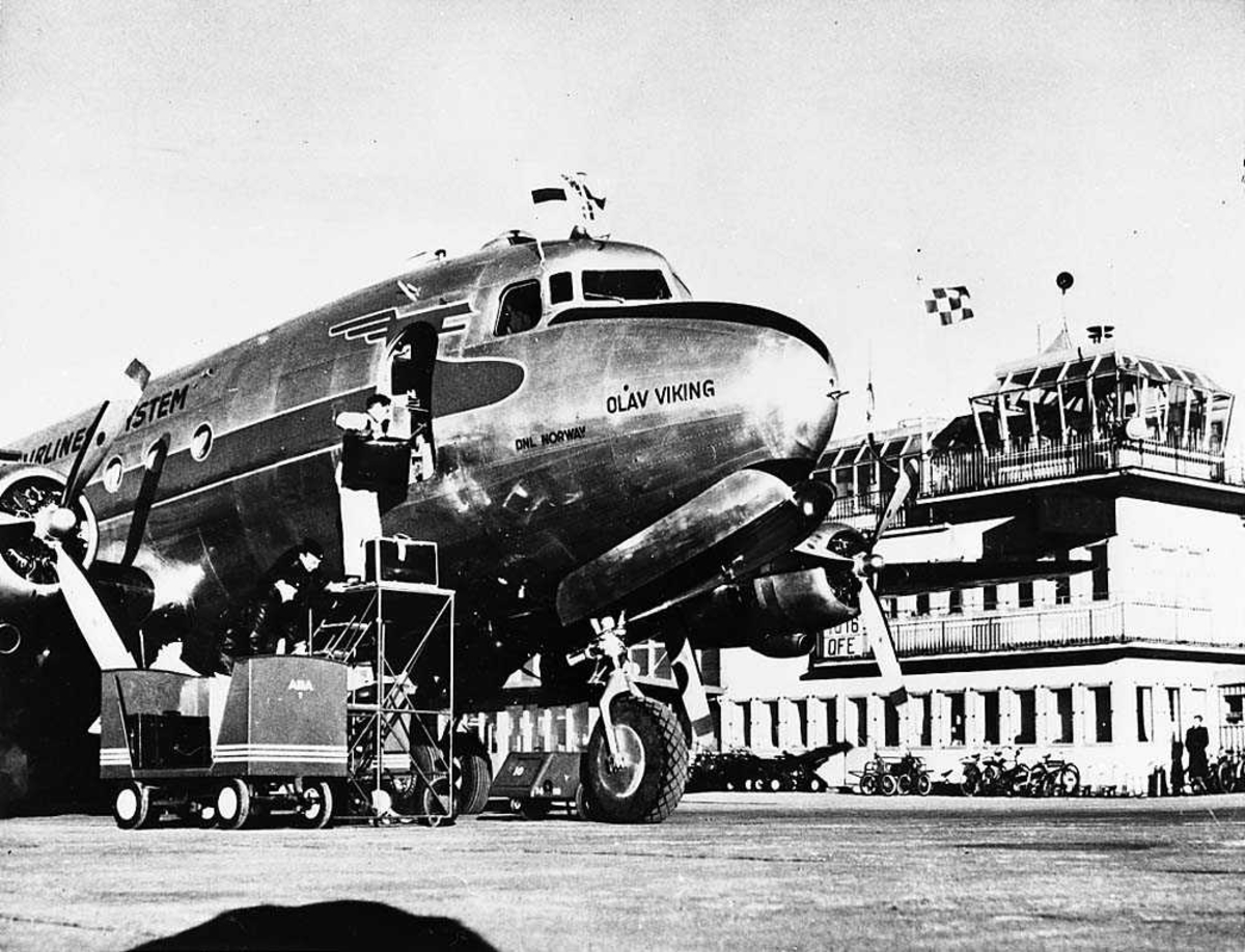 Lufthavn. Ett fly på bakken, Douglas DC-4/C-54 Skymaster "Olav Viking" fra SAS. Bygning i bakgrunnen.