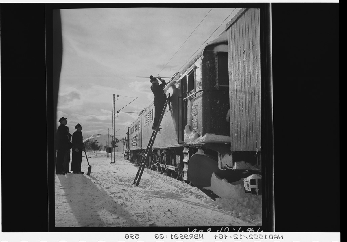 Jernbanepersonell fjerner snø fra lokomotiv. Loket er et elektrisk lokomotiv av type El.3.