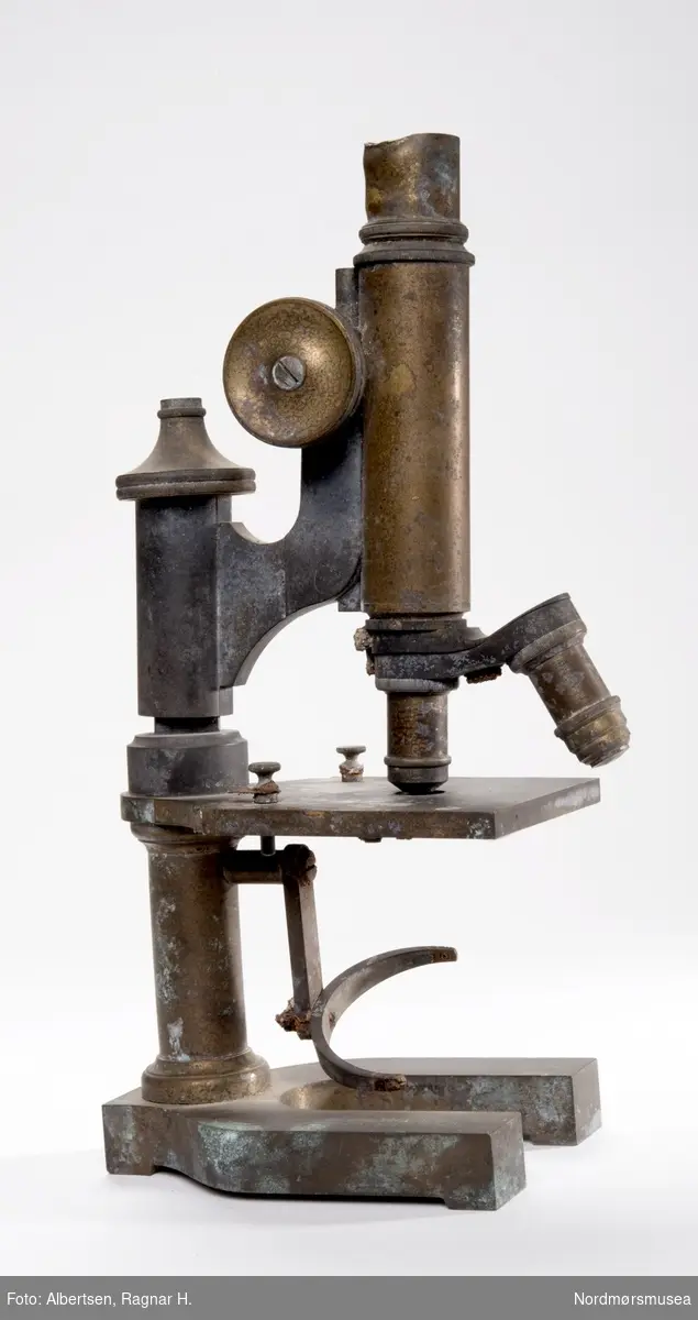 PROT: Et mikroskop funnet i branntomten på Høyere skoles trebygnings ruiner. Kjøpt til skolen i 1900 - det nyeste mokroskopet skolen hadde. (Prot.C.109). 
Hesteskoformet sokkel.