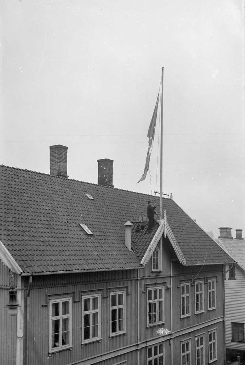 Det gamle rådhuset i Haugesund. En mann står på taket og heiser flagg med byvåpenet.