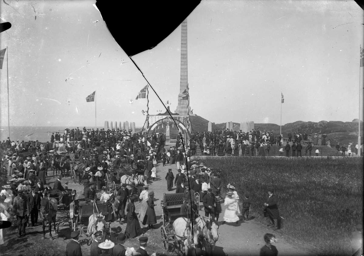 Kongeinntoget på Haraldshaugen den 26. juli i 1906. Haraldshaugen med flagg midt på bildet. Flere hester med vogn midt på og til venstre. Mange personer i forgrunnen og til venstre mot Haraldshaugen.