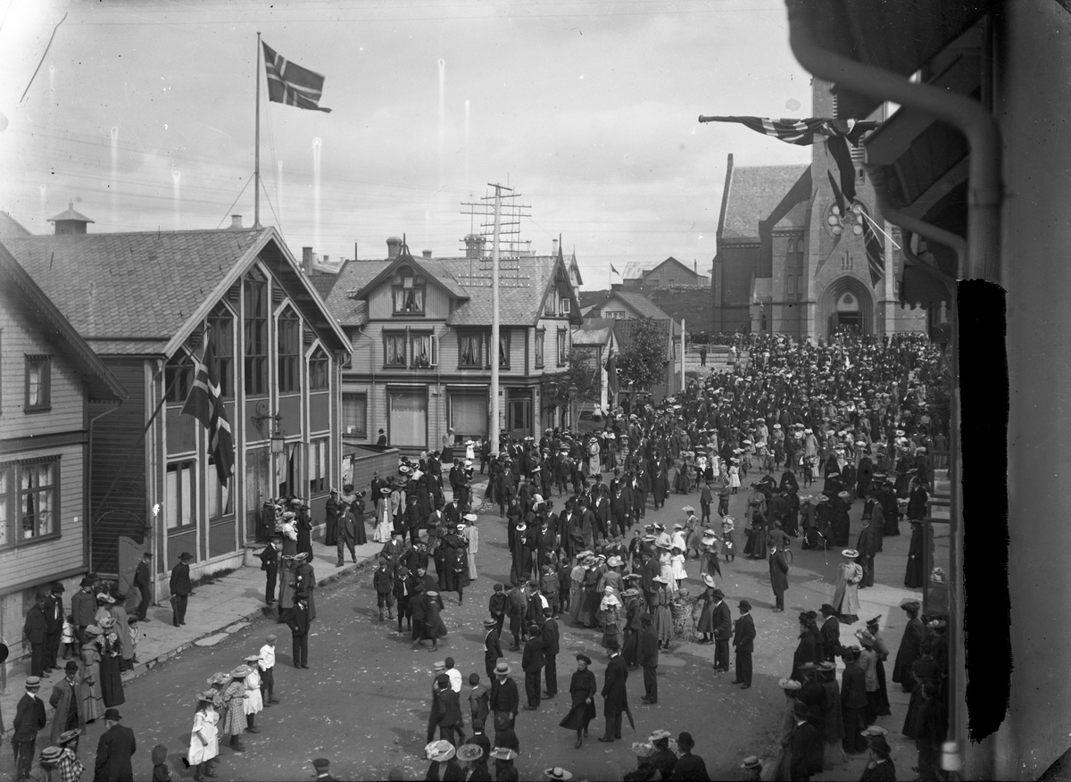 Folketog fra Vår Frelses kirke og vestover den 13.august i 1905 i anledning folkeavstemningen om oppløsningen av unionen med Sverige. Trehus til venstre og i bakgrunnen. Noen norske flagg. Flere personer på gaten.