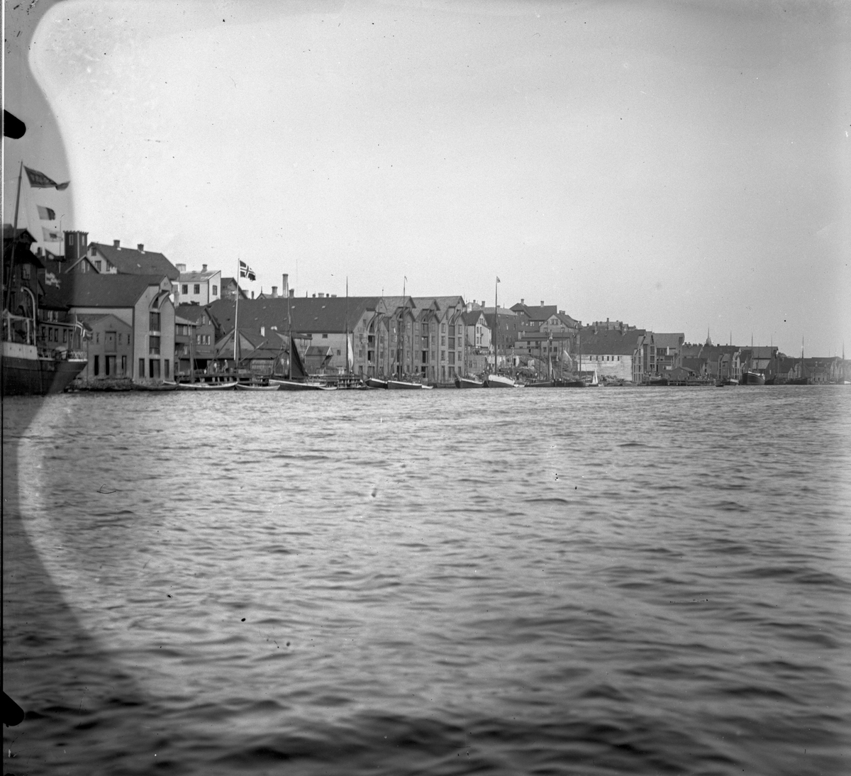 Kaien. Dampskip lengst til venstre.  Flere Fiskebåter, seilfartøy og et dampskip ankret opp ved kai i Smedasundet. Hus og andre bygninger i bakgrunnen. Flaggstang med norsk flagg.