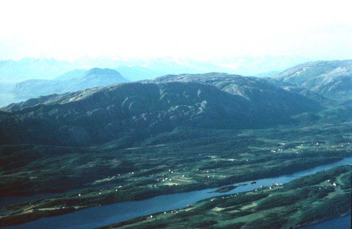Luftfoto. Naturlandskap med ei bygd mellom fjord og fjell sør for Svartisen.