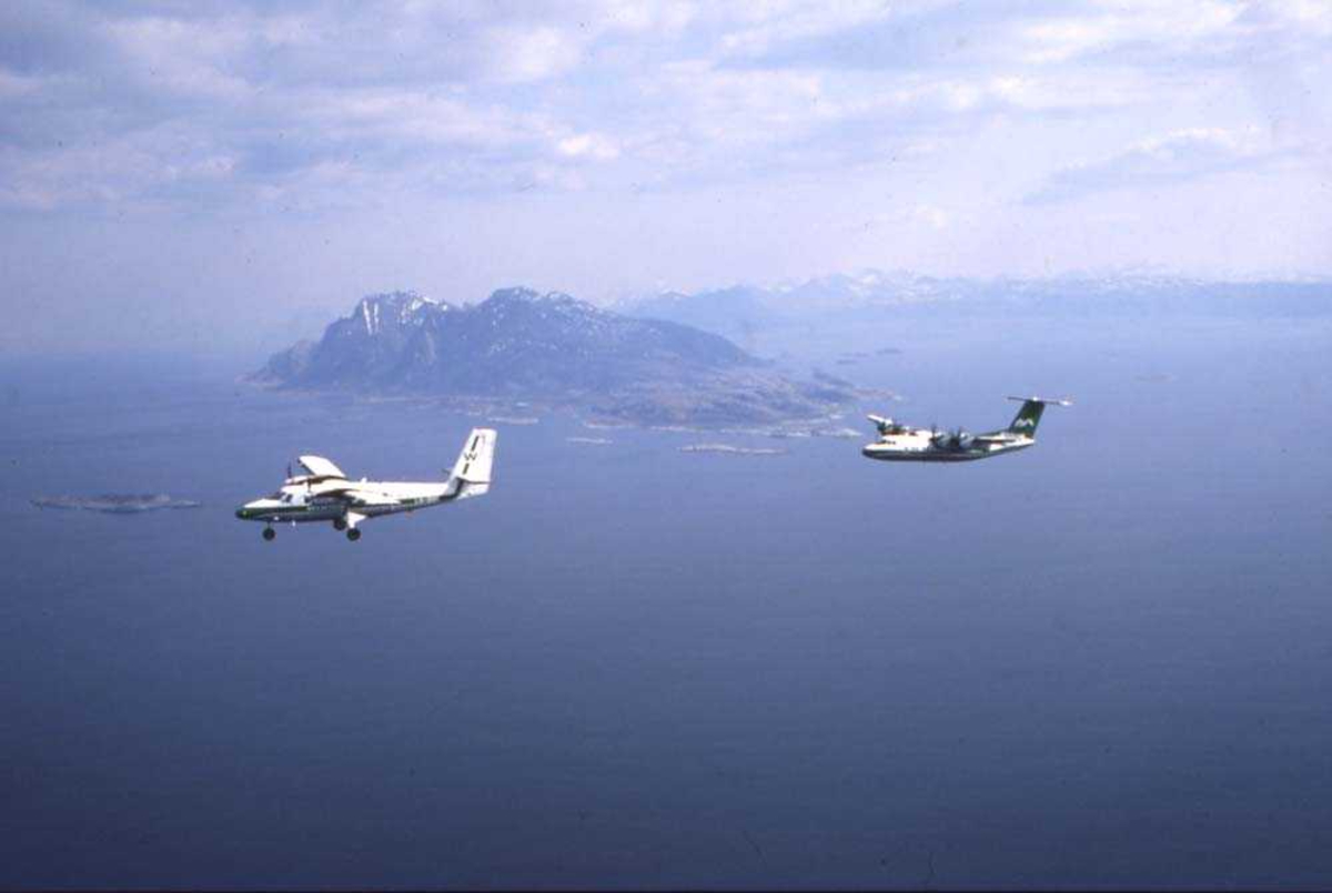 Luftfoto. To fly, LN-WFG, DHC-7-102 Dash7 og LN-BNM, DHC-6-300 Twin Otter fra Widerøe passerer sørenden av Landegode som ses i bakgrunnen.