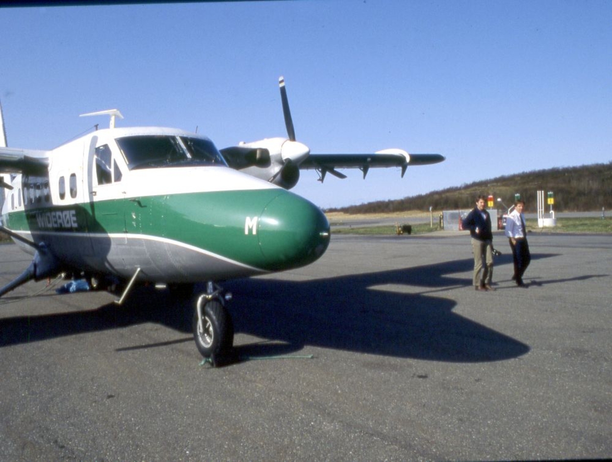 Lufthavn (flyplass). Et fly, LN-BNM, DHC-6-300 Twin Otter fra Widerøe, og to personer som venter på ombordstigning.