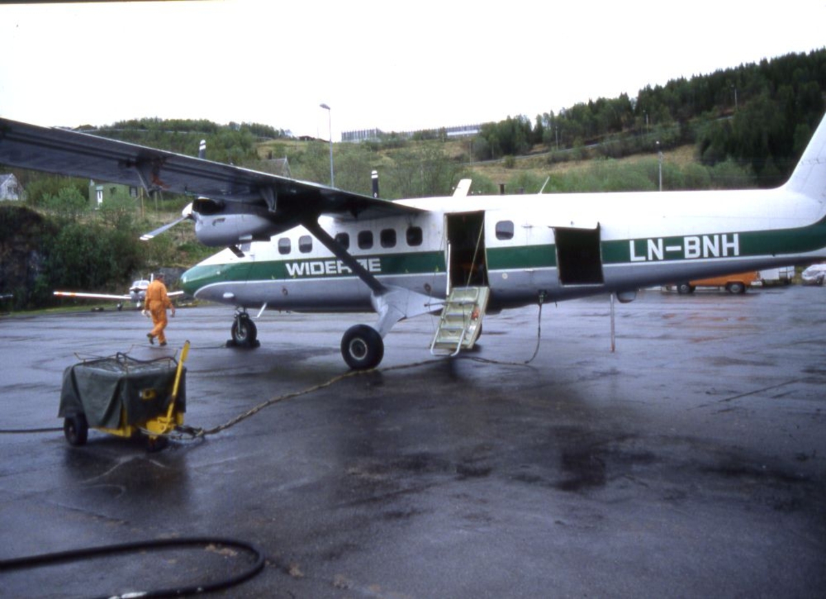 Lufthavn (flyplass). Et fly, LN-BNH, DHC-6-300 Twin Otter fra Widerøe parkert.. En person (lufthavnbetjent) ved flyet.. I forgrunn en startaggregat, Et "småfly" parkert bak Twin Otter.