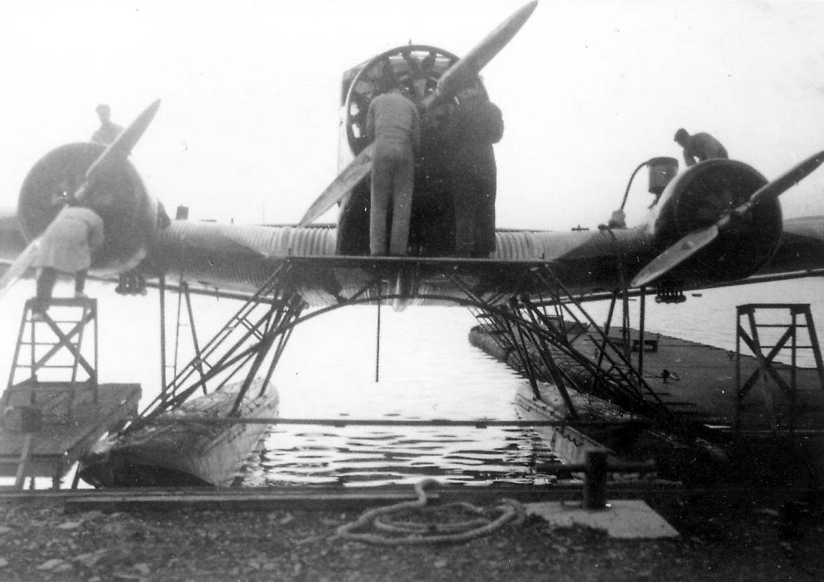 Sjøflyhavn, ett fly i vannkanten, Junkers Ju 52/3mg3e. Flere personer, ant. mekanikere, arbeider med flyet. Flytebrygge/kai.
