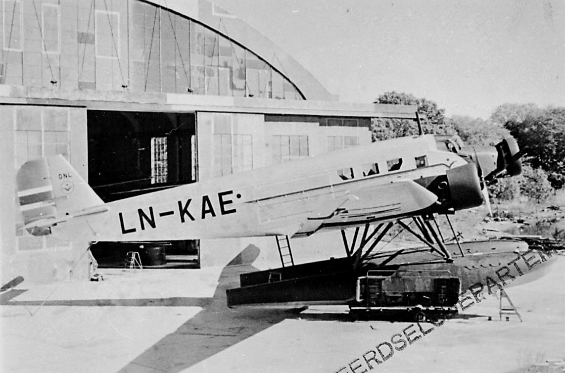 Lufthavn, 1 sjøfly står på land, Junkers JU 52 3mg 7d, LN-KAE "Pål" fra DNL A/S Oslo. 1 hangarbygning i bakgrunnen.