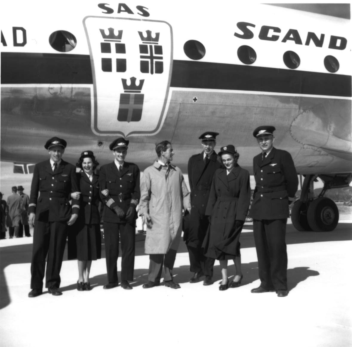 Lufthavn, flere personer oppstilt foran ett fly, DC-4 Skymaster LN-IAD fra SAS. Flypersonell i uniformer og en person i "vanlige" klær.