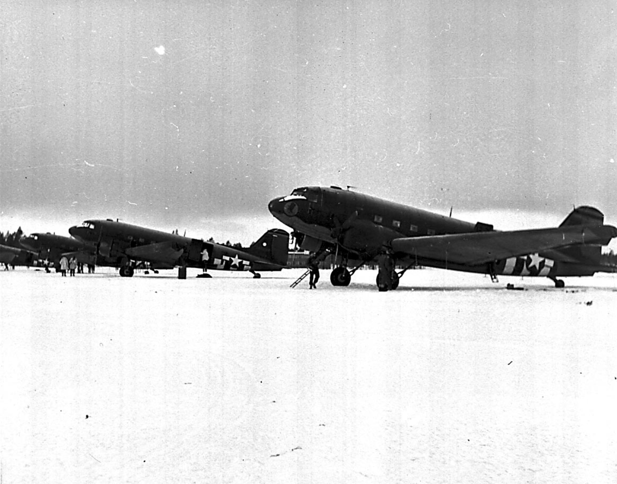 4 fly på bakken, Douglas DC-3/ C-47 Dacota fra USAF. Flere personer ved flyene.