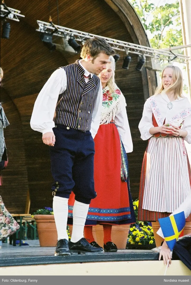Firandet av den svenska nationaldagen den 6 juni 2004 på Skansen. Människor iklädda folkdräkt. Näsby Parks Scoutkår. Blomsterarrangemang.