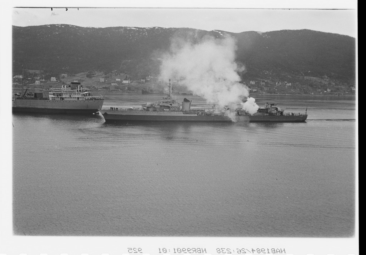Fransk jager Le Terrible ankommer Narvik havn og utveksler salutt med norske marinefartøy. Markering av 6-årsdagen for gjenerobringen av Narvik.I bakgrunnen ses akter til en malmbåt.