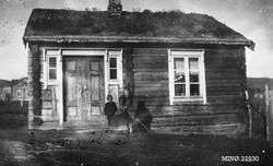 Gutt og kvinne foran lite bolighus