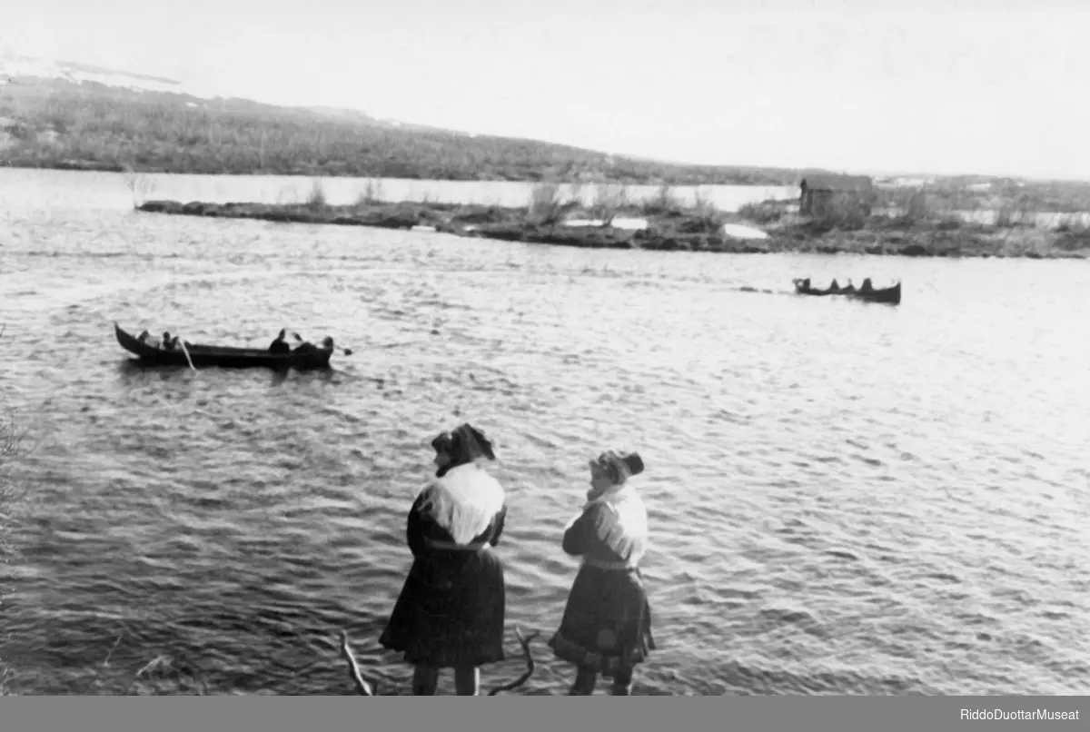 Guokte nieidda várdájit fatnasiid mat oidnojit eanus.
To jenter ser på båtene på elva.