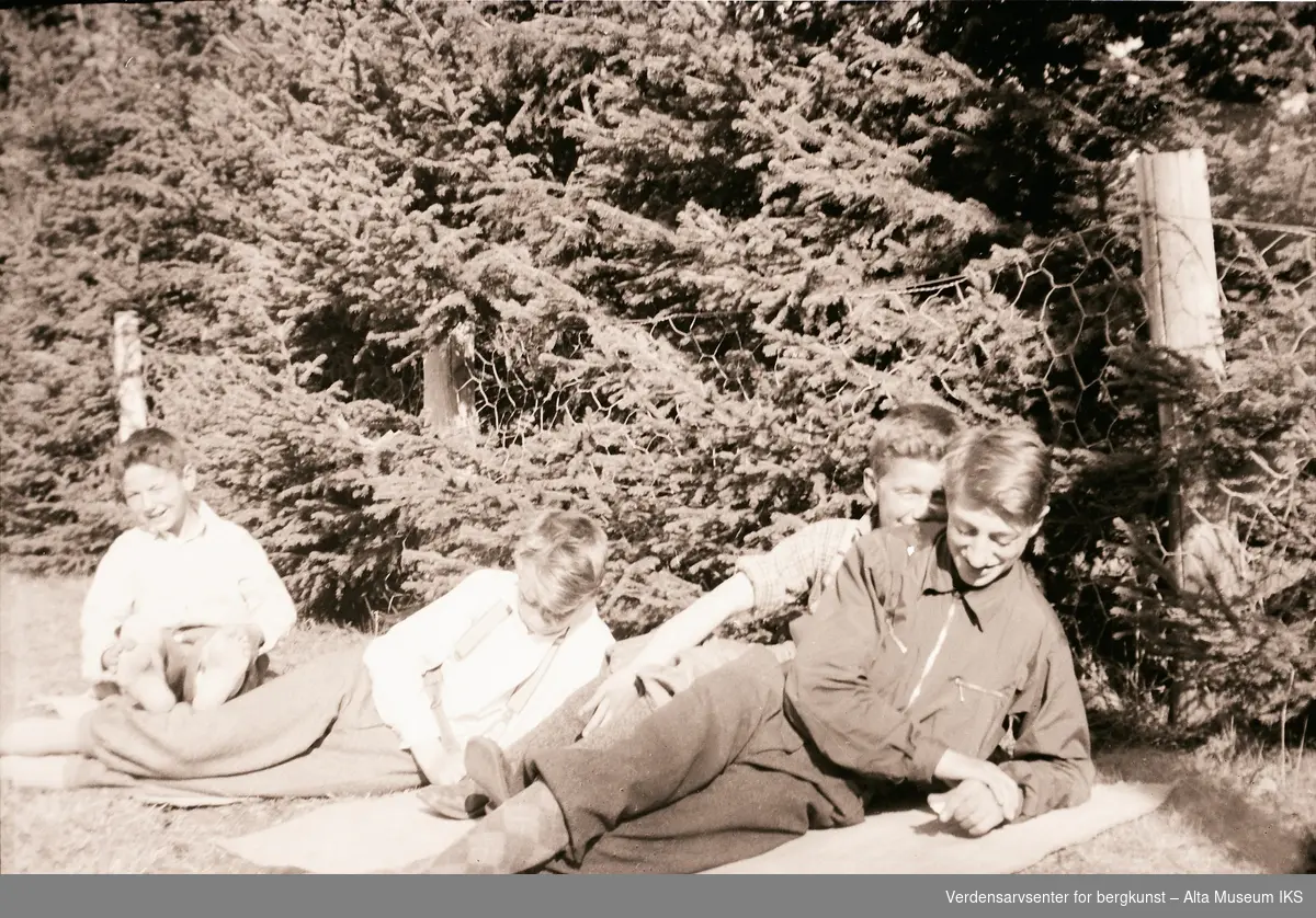 Brødrene Arne, Per og Roar Jøraholmen slapper av på gresset en solfylt dag. Søskenebarnet deres er nærmest kameraet. Bildet er fra Jøraholmen, rundt 1937.
