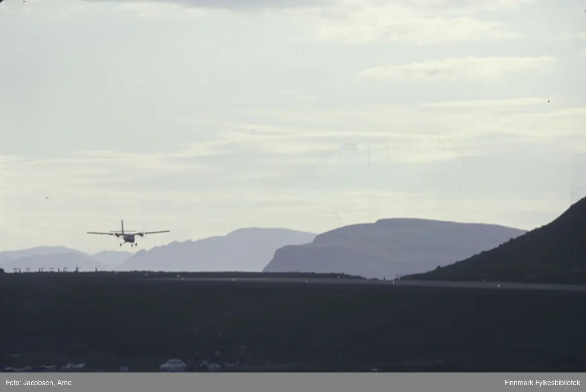 Et Twin Otter-fly fra Widerøes flyveselskap går inn for landing på Hammerfest lufthavn. Toppen av Håja ses omtrent i midten av bildet med enden av Vardfjell foran den. Sørøya lengst bak. En lys bil står parkert nederst på bildet, i nærheten av området Flakket som i dag er lufthavn- og industriområde.