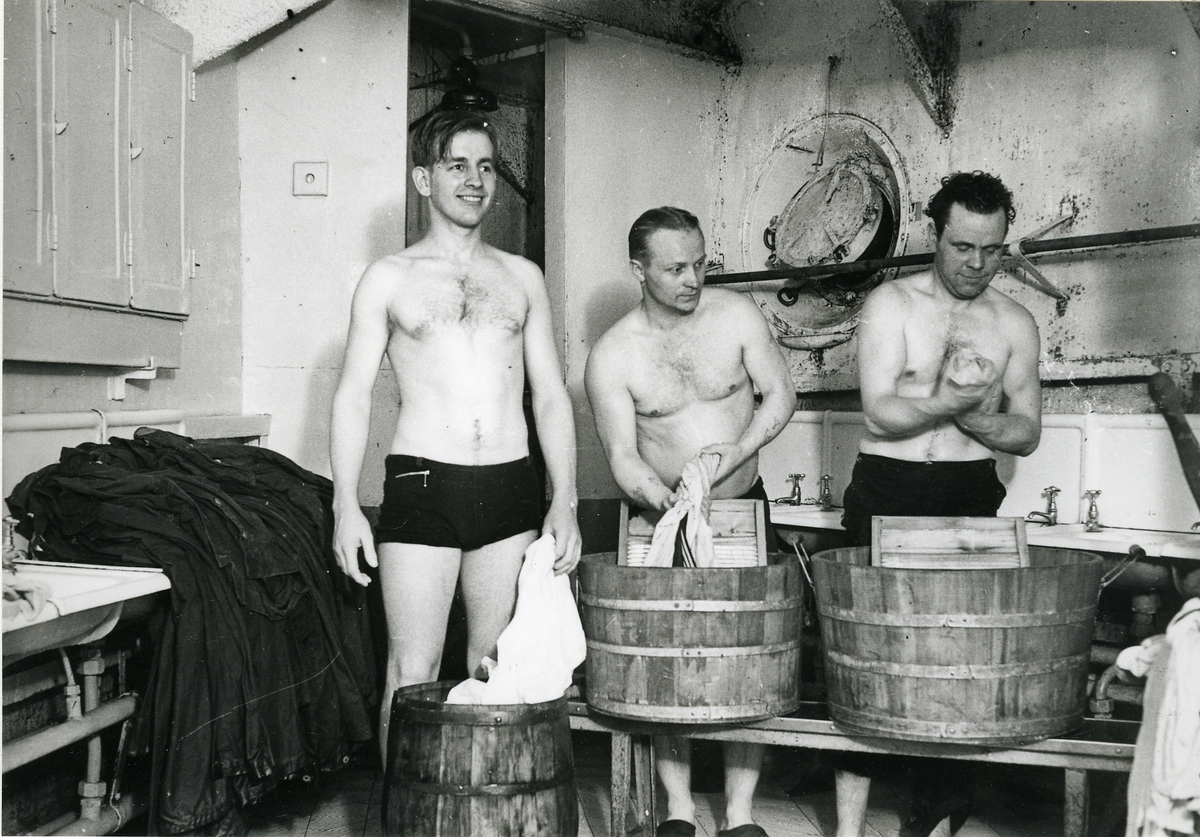 Tre man tvättar kläder i baljor i tvättrummet.