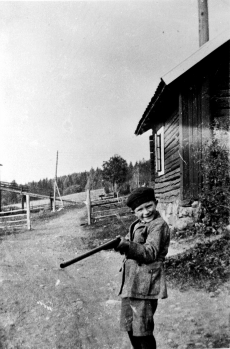Gerhard Vien f.1917 med gevær utenfor gammelt hus på Grimsrud, Helgøya.