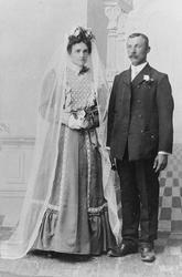 1 brudepar. Bruden er kledd i lang mørk kjole og langt lyst 