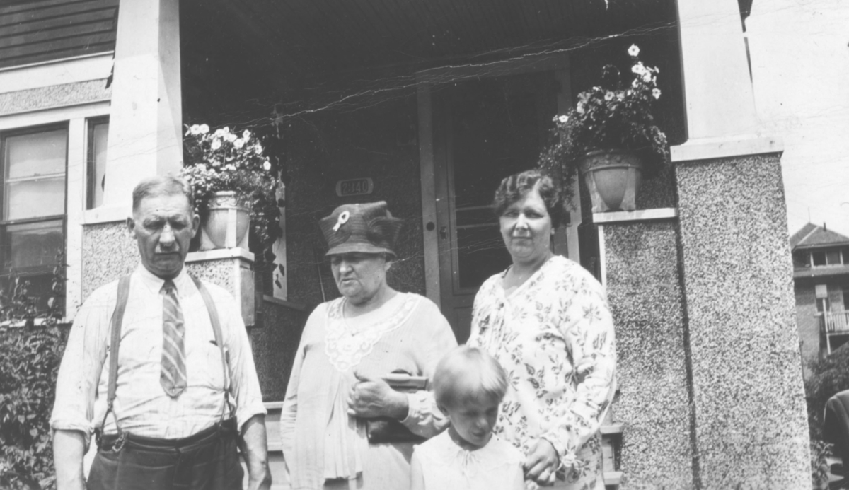 Et gruppebilde av Peter A. Pelto og Ida Johanne Pelto, deres datter Florence og barnebarn Tjai (framst). Peter er kledd i skorte, bukse og slips. Han har også på seg bukseseler. Ida har på seg en hatt, Florence en kjole. I bakgrunnen kan man se huset til en ukjent Wara -person. Inngangen er dekorert med blomsterpotter. Bildet trolig tatt på 1930-tallet (senest 1934). Peter og Ida emigrerte til USA på begynnelsen av 1900-tallet og bodde i Detroit, tilsammens fikk de 11 barn.