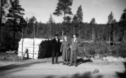 Fotografi av to menn og en kvinne som står på en grusveg. Fr