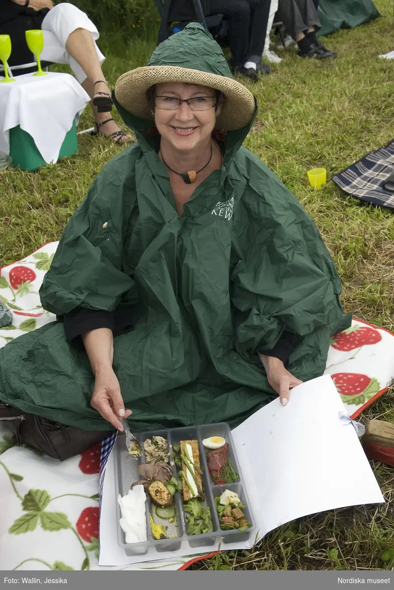 Firande av kronprinsessbröllopet 19 juni 2010, Ockelbo. Kvinna i regncape håller upp en picknicklåda.
