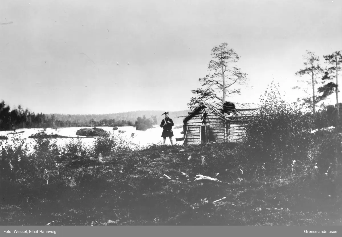 Fra Skogfoss "Männikafoss", september 1896. Ole Johnsen Must står foran koia med en øks over skulderen.