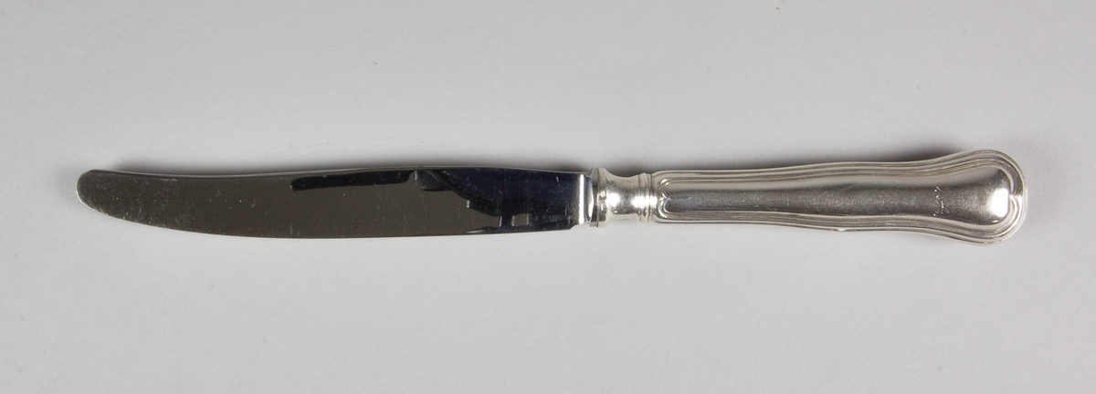 Matkniv av silver med knivblad av stål. På skaftets ovansida löper en kant som i övre änden avslutas i en hjärtformad spets. Med stämplar på skaftets fäste och på skaftets baksida.
