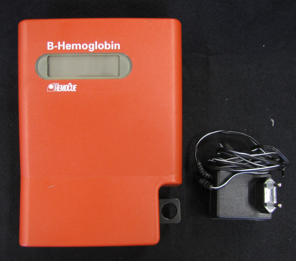 Apparat för mätning av hemoglobin. Apparaten är röd och försedd med en digital panel. Till föremålet finns tillbehör som en fotometer för kalibrering av hb-mätaren samt en behållare med fotometrar för provtagning för att avläsa blodets hb.

Föremålet ingår i en samling med föremål som använt av skolsköterskorna i Vänersborg genom åren.