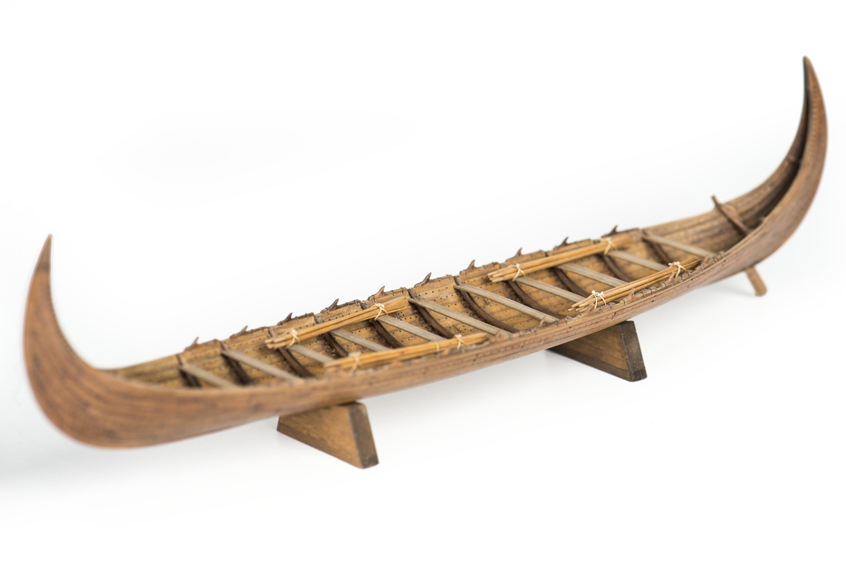 Fartygsmodell av oxelträ, rekonstruktion av "Stora Kvalsundsbåten, utgrävd 1920", daterad till 400-700 e.Kr.. Skrov utfört i två halvor med limfog genom köl och stävar. Bordläggningen skuren på såväl in- som utsidan. Klamparna på borden pålimmade. Håarna av lövträkvistar, med självvuxen knagge, fastbundna med svartoxiderad suturtråd. Skrovet betsat i tjärfärg.